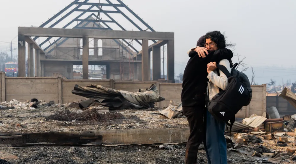 Mirtza Aguilera, right, and her daughter embrace in front of their home burned by wildfires in Tome, Chile, Monday, Jan. 19, 2026. (AP Photo/Javier Torres)