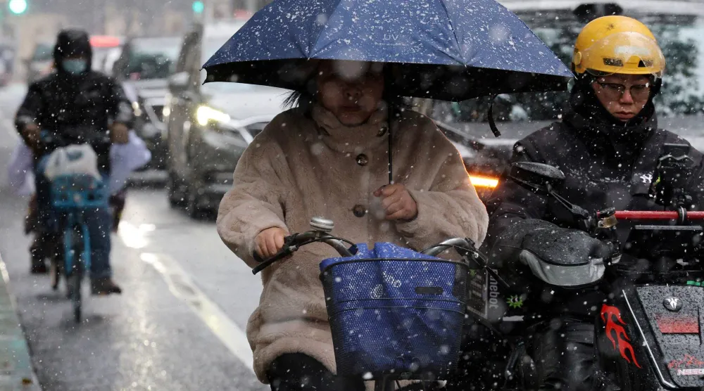 A woman holding an umbrella rides a bicycle amid snowfall in Shanghai, China January 20, 2026. (Reuters)