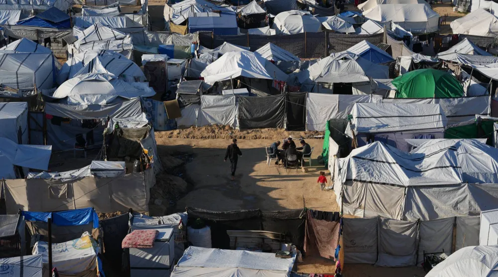 نازحون فلسطينيون يتجمعون خارج خيمة في مخيم مؤقت بمدينة دير البلح في وسط قطاع غزة (أ.ب)