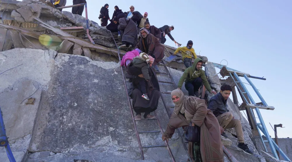 سكان يحاولون عبور جسر متضرر (بفعل «قسد» حسب رواية الجيش السوري) في الرقة أمس (رويترز)