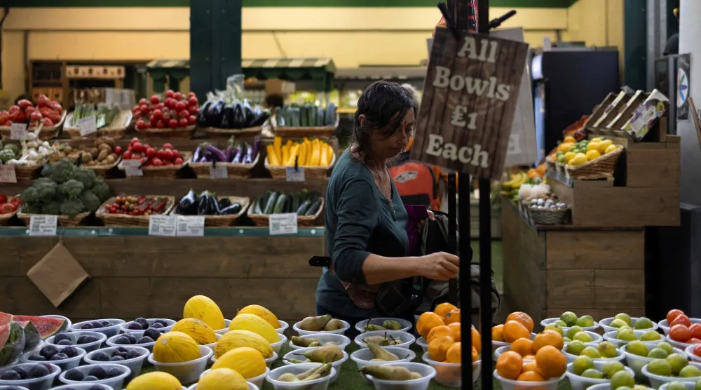 امرأة تشتري فواكه وخضراوات في السوق المحلية بمدينة برايتون (رويترز)