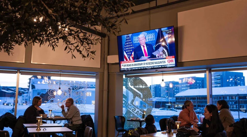 يجلس أشخاص داخل مقهى في نوك بغرينلاند بينما تُظهر شاشة تلفزيونية الرئيس الأميركي دونالد ترمب يوم 20 يناير 2026 (أ.ف.ب)