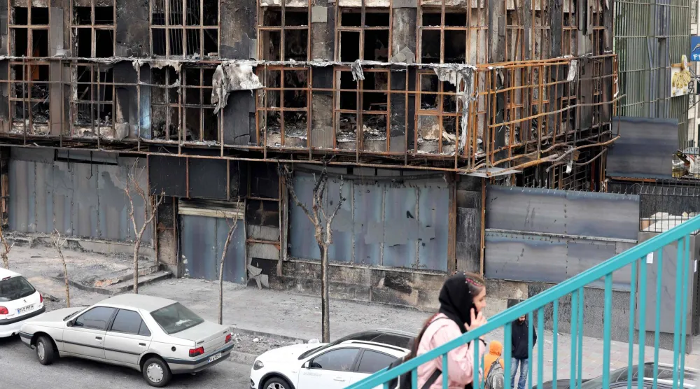 امرأة تمشي فوق جسر بجوار مبنى محترق دمر خلال الاحتجاجات العامة في طهران (أ.ف.ب)