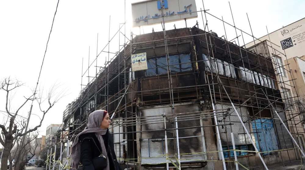 إيرانية تمر أمام فرع لبنك صادرات تضرر جراء حريق اندلع خلال الاحتجاجات (إ.ب.أ)