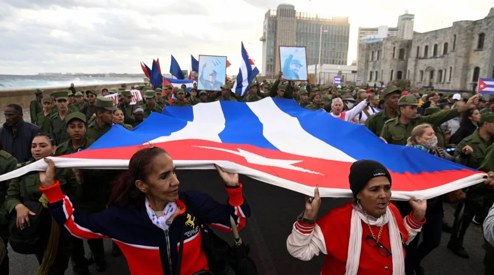 عسكريون ومدنيون يحملون علماً كوبياً كبيراً خلال مسيرة أمام السفارة الأميركية احتجاجاً على ما وصفوه بـ«العدوان الأميركي» في المنطقة (رويترز)