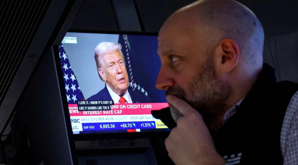 شاشة تعرض دونالد ترمب وهو يجري مقابلة خلال اجتماع المنتدى الاقتصادي العالمي في دافوس بينما يعمل أحد المتداولين بقاعة بورصة نيويورك (رويترز)