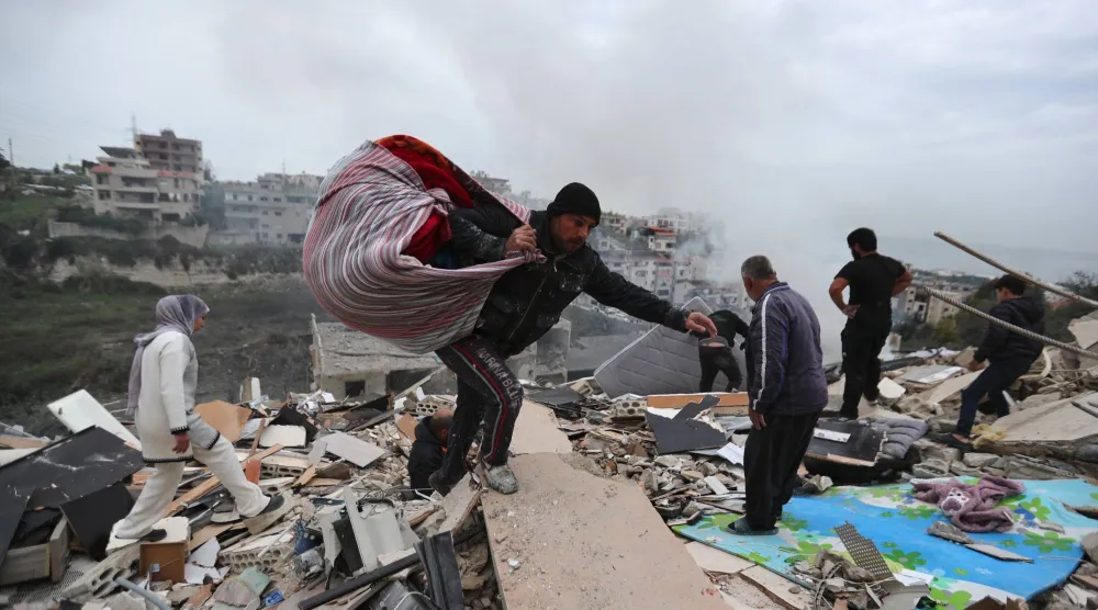 مواطنون يجمعون ما تبقّى من أغراضهم على أثر استهداف المبنى الذي يسكنون فيها ببلدة قناريت بجنوب لبنان مساء الأربعاء (أ.ب)