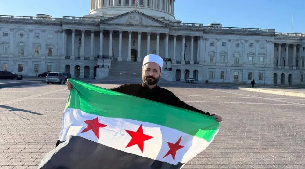 سليمان عبد الباقي مدير الأمن الداخلي في السويداء يرفع العلم السوري أمام مبنى الكونغرس في واشنطن (إكس)