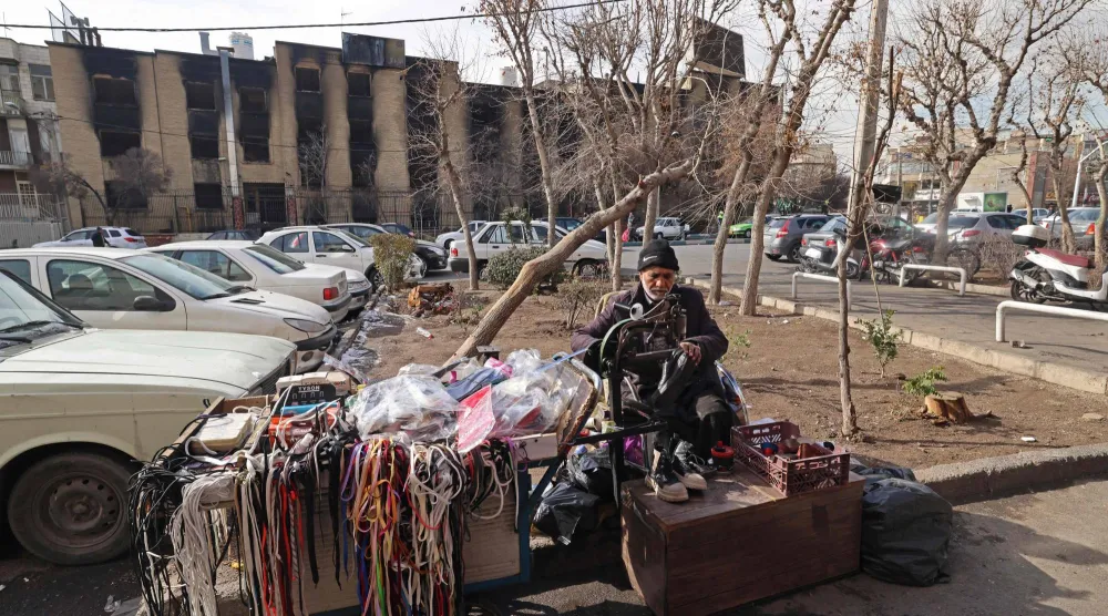 إسكافي يصلح أحذية يجلس أمام مبانٍ حكومية احترقت خلال الاحتجاجات العامة الأخيرة في طهران (أ.ف.ب)