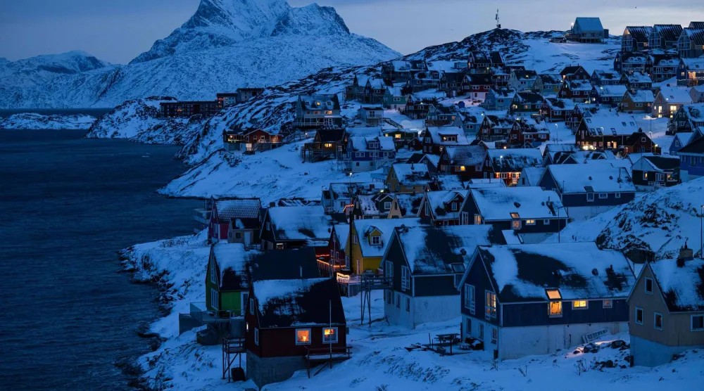 منازل مضاءة على طول الساحل مع بزوغ ضوء الصباح الباكر فوق التلال المغطاة بالثلوج في نوك بغرينلاند 22 يناير 2026 (أ.ف.ب)