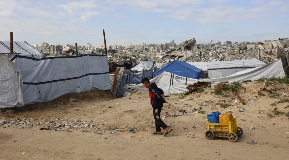 طفل فلسطيني يسحب حاويات مليئة بالماء في مخيم جباليا للاجئين شمال قطاع غزة (أ.ف.ب)