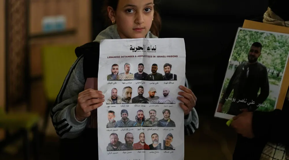 فتاة تحمل صور 20 أسيراً من «حزب الله» لدى إسرائيل خلال وقفة تضامنية نظمها الحزب دعماً لهم في الضاحية الجنوبية يوم الأحد (أ.ب)