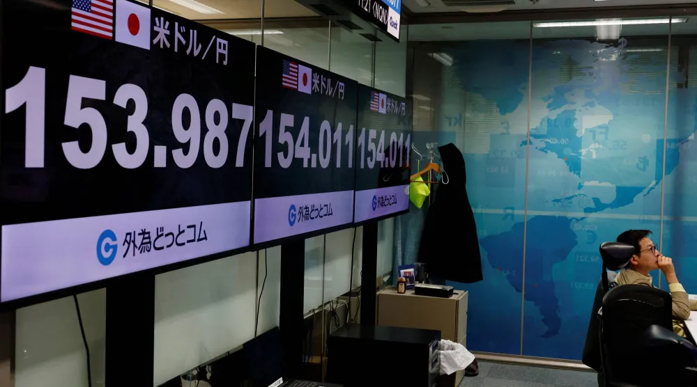 موظف في شركة لتداول العملات الأجنبية يعمل أمام شاشات تعرض سعر صرف الين الياباني مقابل الدولار الأميركي (رويترز)