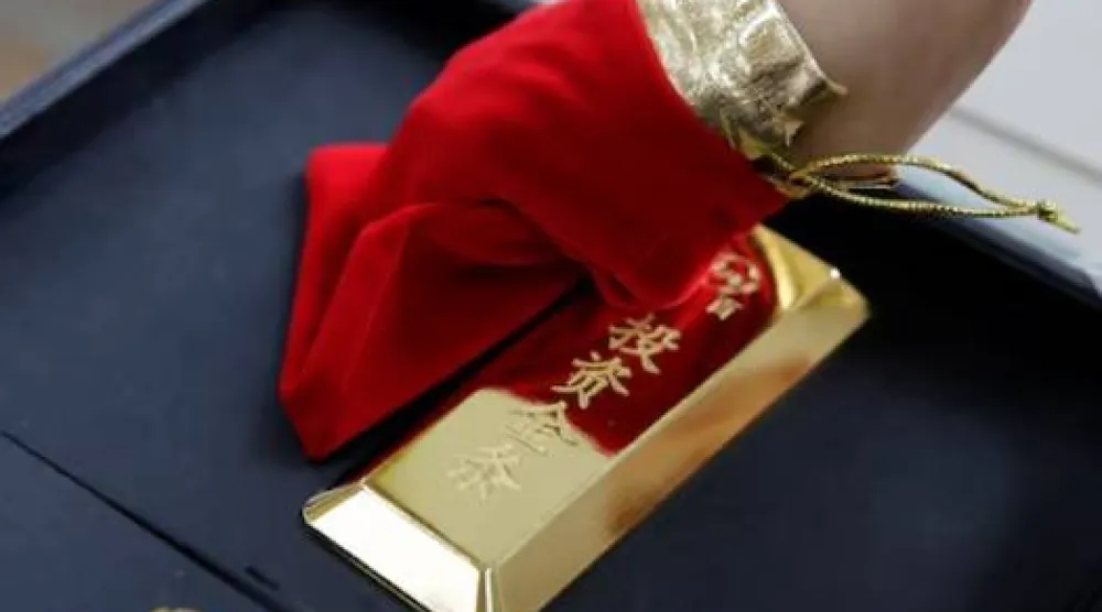 مساعد مبيعات يعرض سبيكة ذهبية في متجر كايباي للمجوهرات ببكين (رويترز)