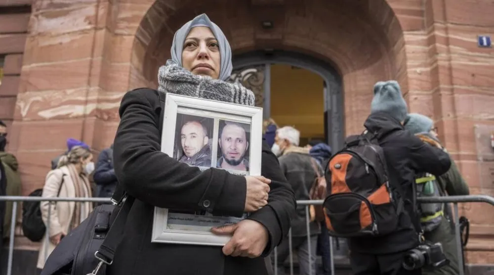 الناشطة السورية ياسمين المشعان تحمل صور ضحايا لنظام الرئيس بشار الأسد أمام محكمة في ألمانيا يوم 13 يناير 2022 (أرشيفية - أ.ف.ب)