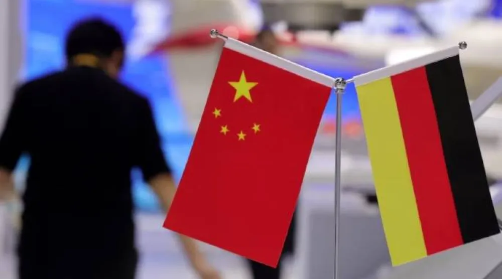 شخص يسير بجانب علمي الصين وألمانيا خلال الدورة الثامنة للمعرض الدولي الصيني للاستيراد في شنغهاي (رويترز)