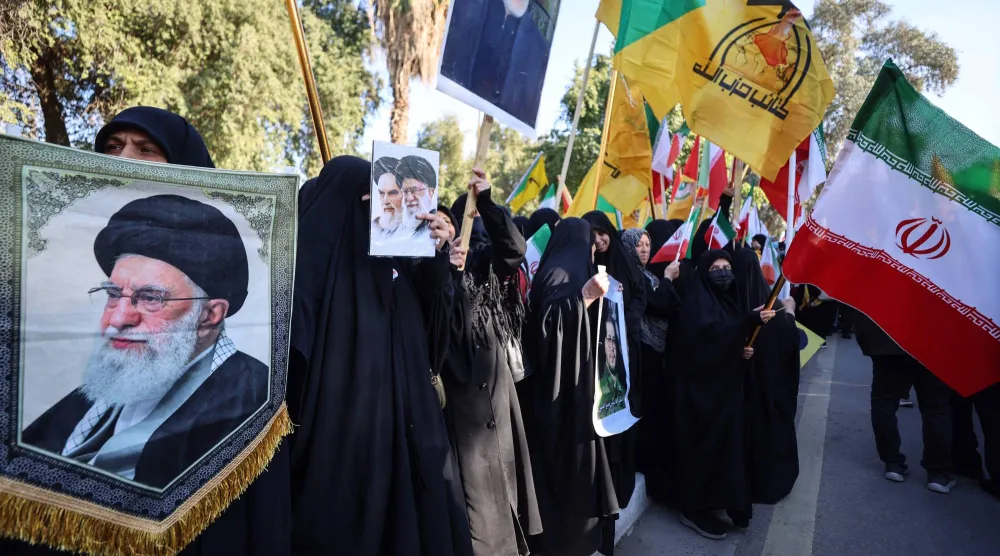 عراقيون يحملون علم إيران وشعار «كتائب حزب الله» وصورة خامنئي خلال مظاهرة في بغداد (أ.ف.ب)