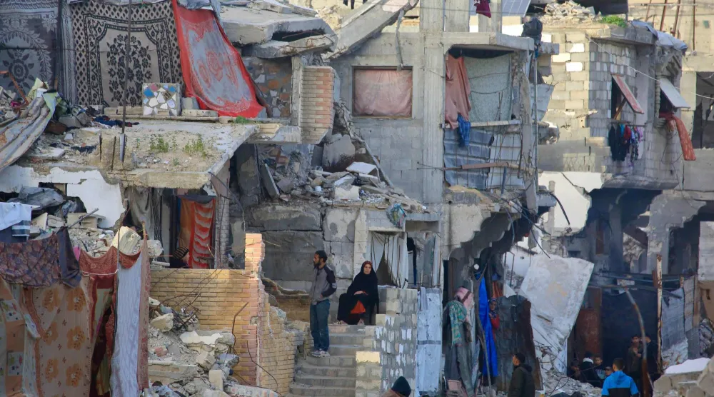 فلسطينيون يجلسون وسط المنازل المدمرة في خان يونس (أ.ف.ب)