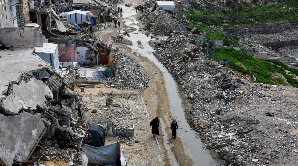 فلسطينيون يسيرون يوم الأربعاء بين أنقاض المباني السكنية التي دمرتها إسرائيل في مدينة غزة (رويترز)