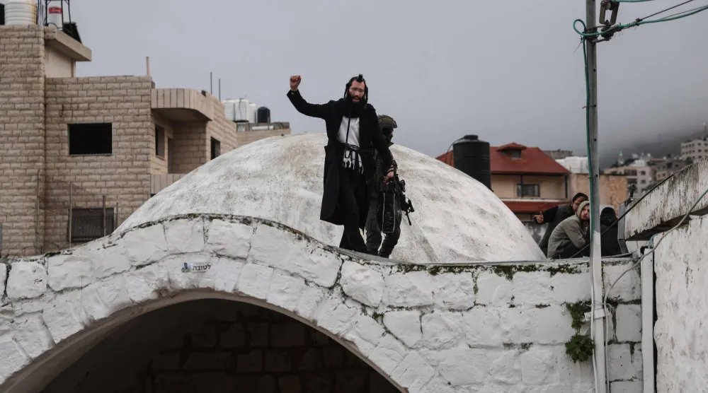 يهودي يلوّح فوق قبر يوسف بمدينة نابلس في شمال الضفة الغربية المحتلة (أ.ف.ب)