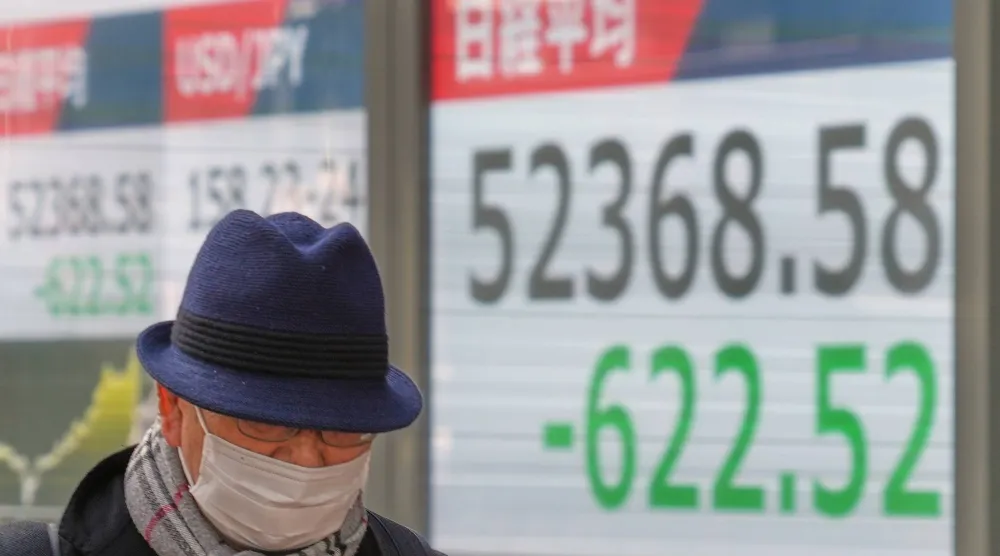 رجل يمر أمام شاشة تعرض حركة الأسهم في وسط العاصمة اليابانية طوكيو (أ ب)