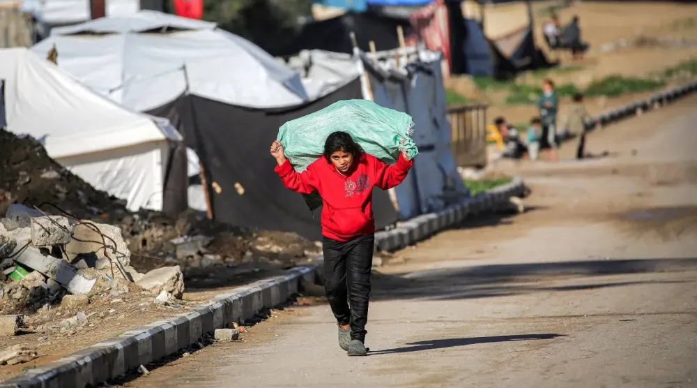 Gazze Şeridi'nin orta kesimindeki Deyr el-Balah'ın kuzeyinde bulunan Nuseyrat Mülteci Kampı’nda, sırtında çuval taşıyan bir kız çocuğu (AFP)