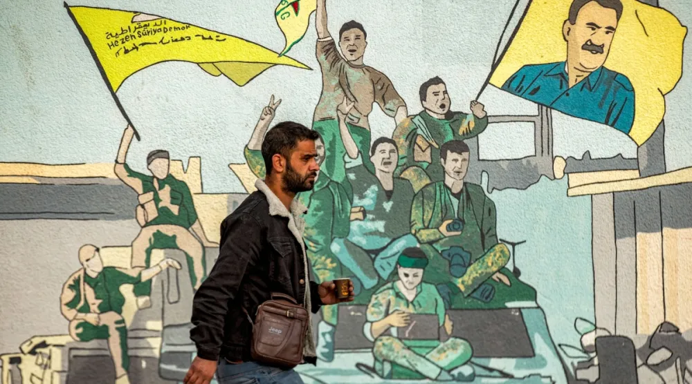 Kamışlı'da Abdullah Öcalan'ın resmini tutan SDG destekçilerinin çizildiği bir duvar resminin önünden geçen bir adam, 16 Aralık 2024 (AFP)