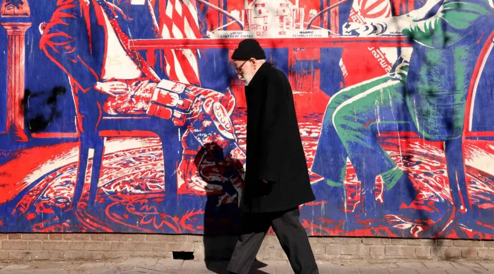 Yetkililerin ‘casus yuvası’ olarak adlandırdığı Tahran'daki ABD Büyükelçiliği’nin dış duvarlarında kan lekeli bir müzakere masasını tasvir eden duvar resminin önünden geçen bir adam (AFP)
