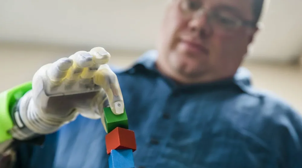 شخص يستخدم يده الاصطناعية لالتقاط مكعب صغير (جامعة ميشيغان)