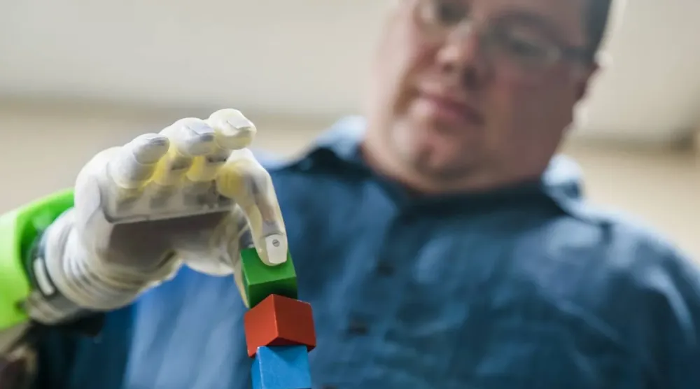 Geliştirilen protez eliyle küçük bir küpü kavrama çalışan bir kişi (Michigan Üniversitesi)