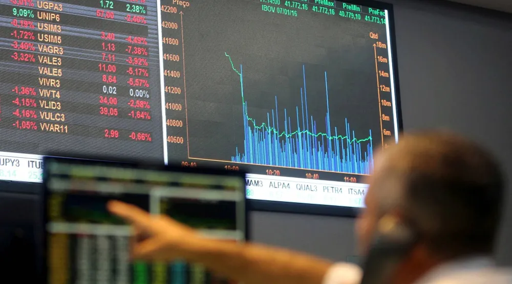 رجل يشير إلى لوحة إلكترونية تُظهر تقلبات مؤشرات السوق في قاعة بورصة بوفيسبا وسط ساو باولو بالبرازيل (أرشيفية- رويترز)