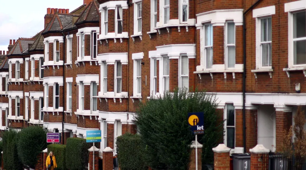 امرأة تمر بجوار منازل معروضة للإيجار في شارع سكني بلندن (رويترز)