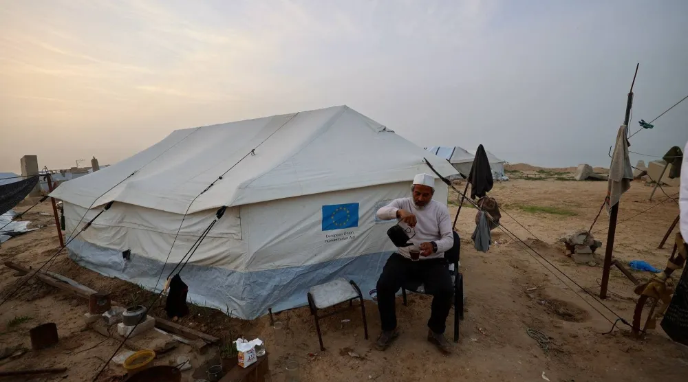 رجل يسكب مشروباً ساخناً خارج خيمة في مخيم النصيرات للاجئين الفلسطينيين وسط قطاع غزة (أ.ف.ب)