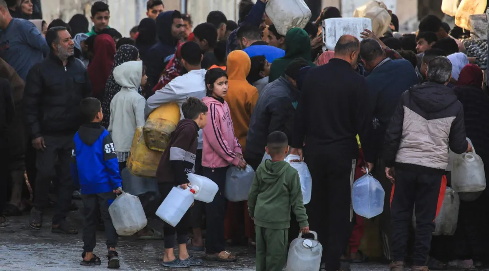 نازحون يتدافعون لملء أوعية بلاستيكية بالماء من منشأة لتكرير الماء في خان يونس السبت (أ.ف.ب)