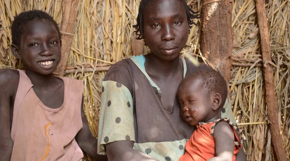 أم فرَّت مع طفليها من الحرب بالسودان تجلس في مخيم ثوبو (رويترز)