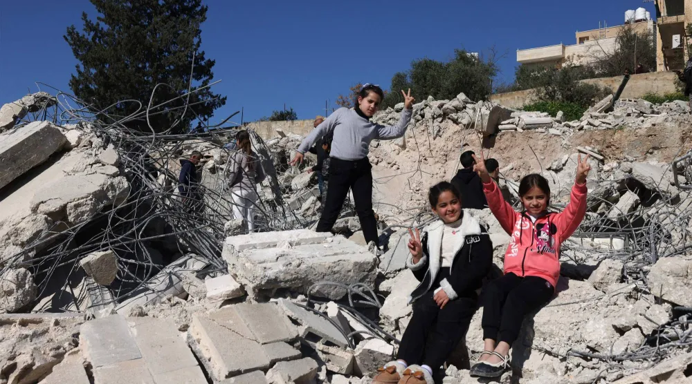 فتيات فلسطينيات يرفعن علامة النصر على أنقاض مبانٍ هدمتها إسرائيل في بيت عوا بمدينة الخليل بالضفة الغربية (أ.ف.ب)