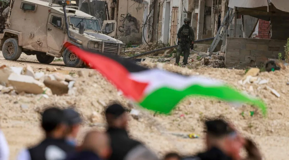 فلسطينيون يتظاهرون أمام جنود إسرائيليين أغلقوا مدخل مخيم نور شمس في الضفة الغربية (أ.ف.ب)