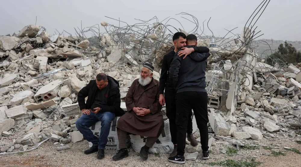 فلسطيني يواسي مواطنه بينما يجلس آخران بين أنقاض منزل هدمته إسرائيل في قرية شقبة غرب مدينة رام الله أمس (أ.ف.ب)
