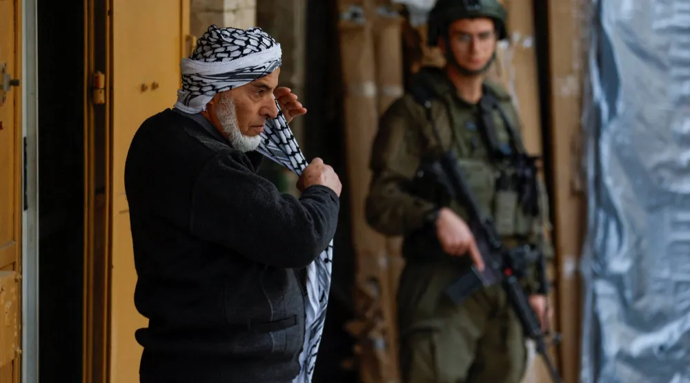 رجل فلسطيني يقف أمام جندي إسرائيلي في مدينة الخليل بالضفة الغربية المحتلة (رويترز)