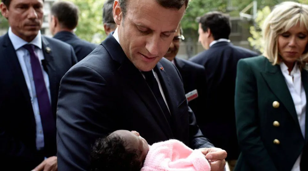 الرئيس الفرنسي إيمانويل ماكرون برفقة زوجته بريجيت يحمل رضيعة خلال زيارته لمستشفى روبرت ديبري للأطفال في باريس (رويترز)