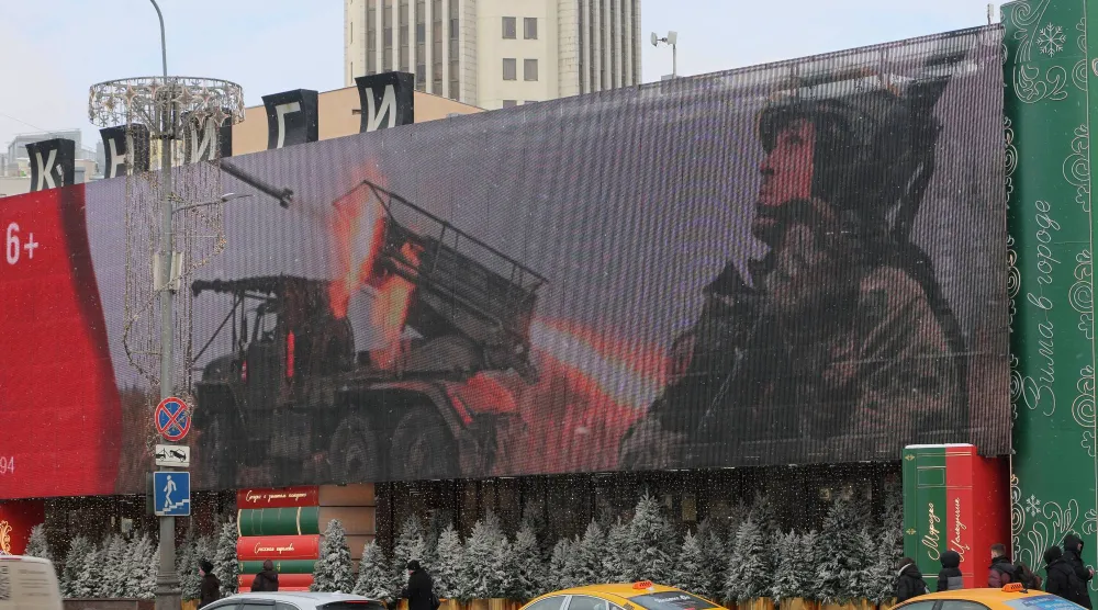 أشخاص يسيرون في أحد شوارع المدينة في موسكو بينما تعرض شاشة إلكترونية صورة جندي روسي (إ.ب.أ)