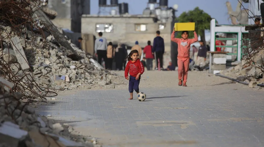 فتاة فلسطينية تلعب بكرة القدم في الشارع بجوار أنقاض المباني المدمرة على يد الجيش الإسرائيلي في خان يونس جنوب قطاع غزة (أ.ف.ب)