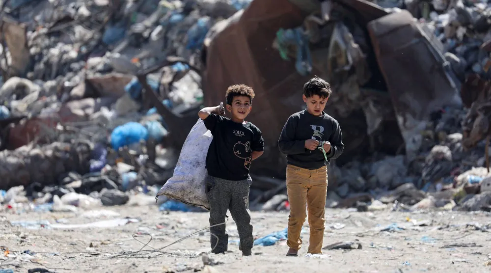 طفلان فلسطينيان يسيران قرب مكب نفايات في مدينة غزة يوم الأربعاء (رويترز)