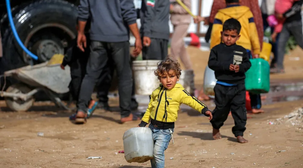 طفل يسير حاملاً وعاء ماء بعد أن ملأه من خزان مياه متنقل في مخيم المغازي للاجئين الفلسطينيين وسط قطاع غزة (أ.ف.ب)
