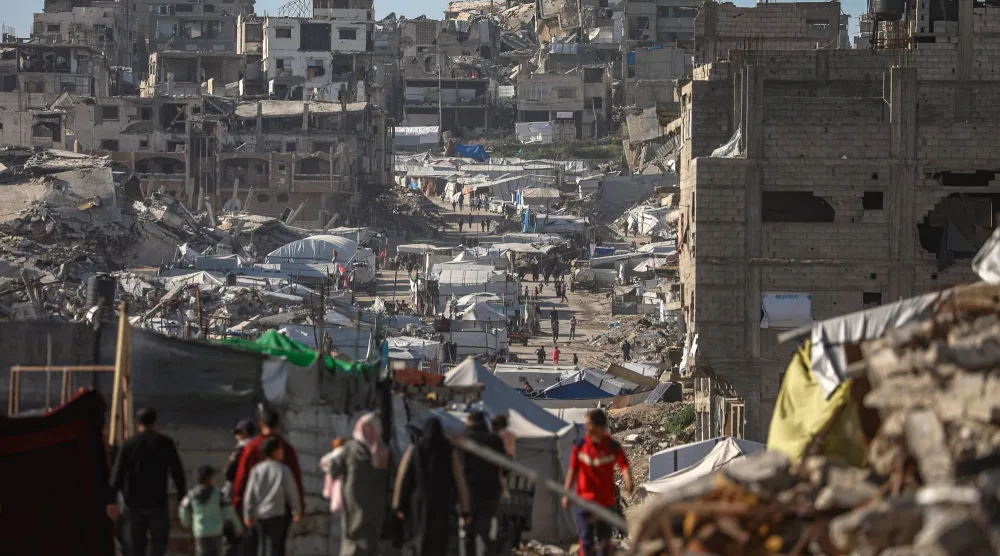 فلسطينيون نازحون داخلياً يسيرون بين أنقاض حي التفاح شرق مدينة غزة (إ.ب.أ)