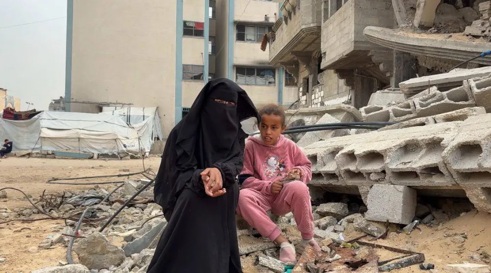 ضحى أبو سنيمة ووالدتها تجلسان بجوار منزل مهدم (الشرق الأوسط)