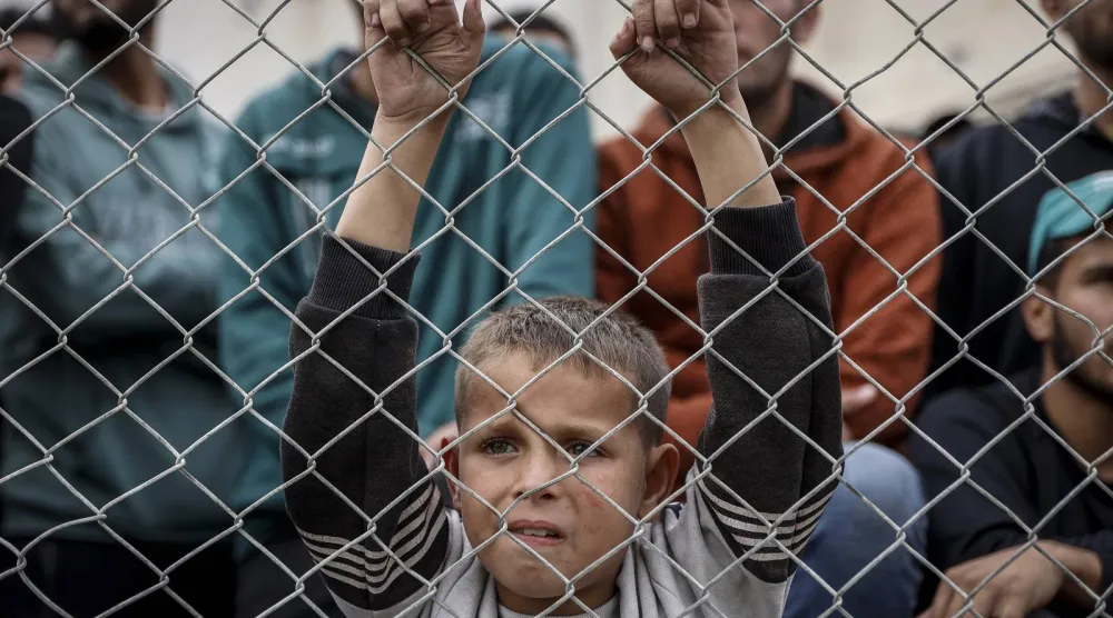 طفل فلسطيني يقف خلف سلك بلاستيكي وسط أنقاض المباني المدمرة في مدينة غزة (أ.ف.ب)