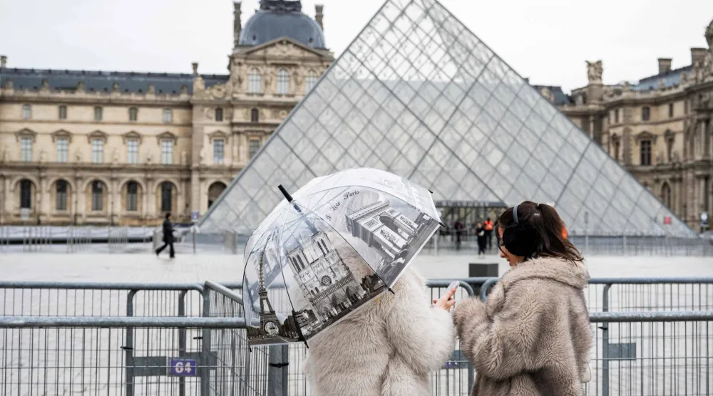 (FILES) Tourists stand next to barriers blocking the plaza with the Louvre Pyramid. (Photo by Martin LELIEVRE / AFP) 