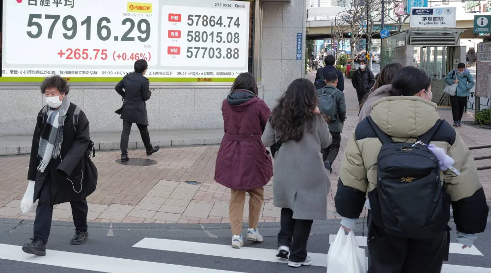 مشاة يعبرون الطريق أمام لوحة تعرض حركة الأسهم في وسط العاصمة اليابانية طوكيو (أ.ب)