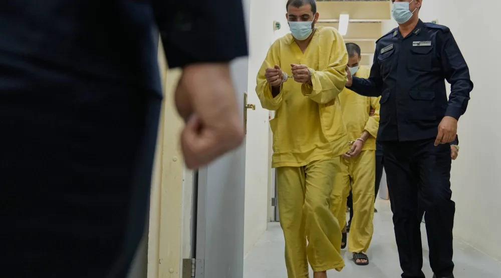 رجل أمن عراقي مع مشتبهين بالانتماء إلى «داعش» في سجن الكرخ ببغداد (أ.ب)